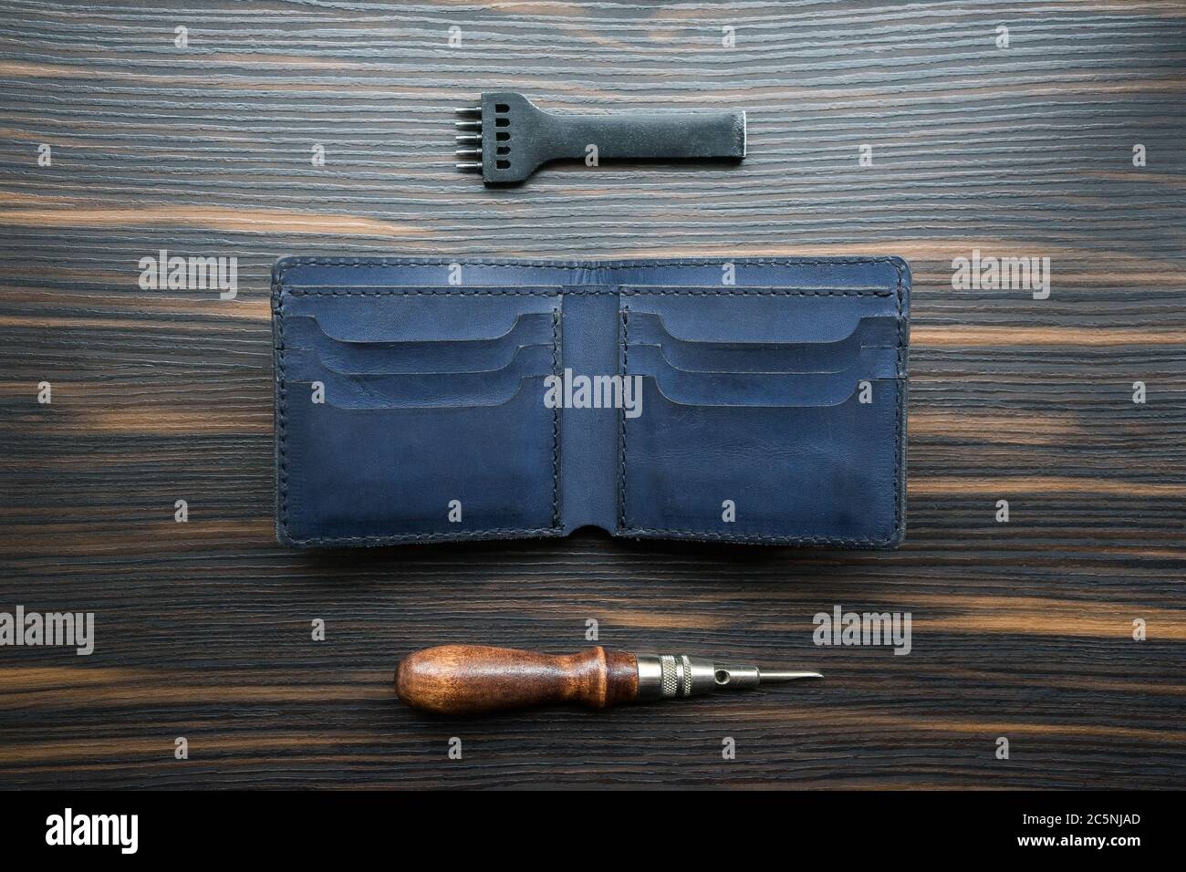handmade blue leather wallet, punch and awl on a wooden table.  Stock Photo