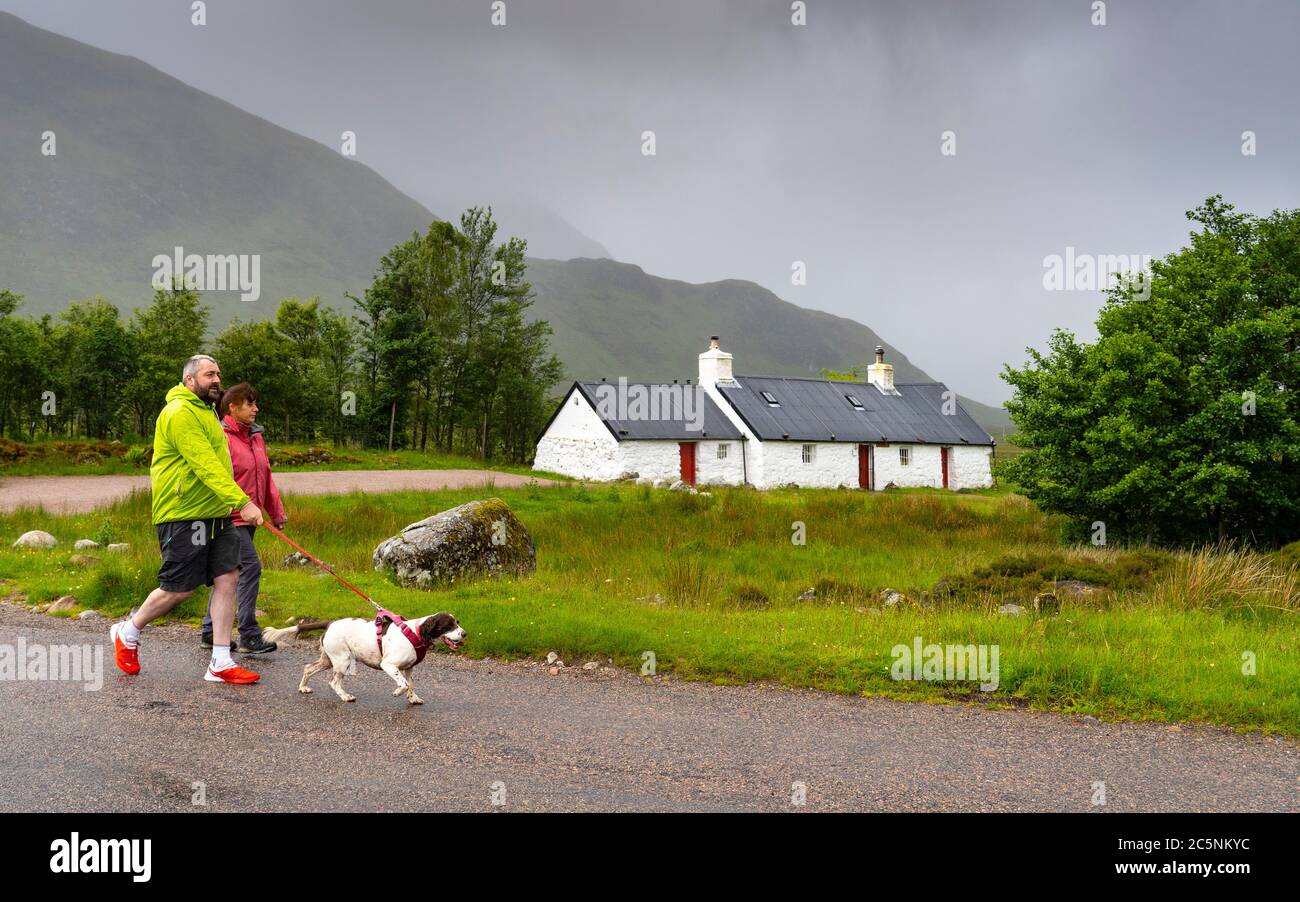 Glen Coe, Scotland, UK. 4 July, 2020. Tourists travel to Glen Coe on first weekend after 5 mile travel restriction was lifted by the Scottish Government. Pictured; Couple walking dog at Blackrock Cottage at Glen Coe ski area. Iain Masterton/Alamy Live News Stock Photo