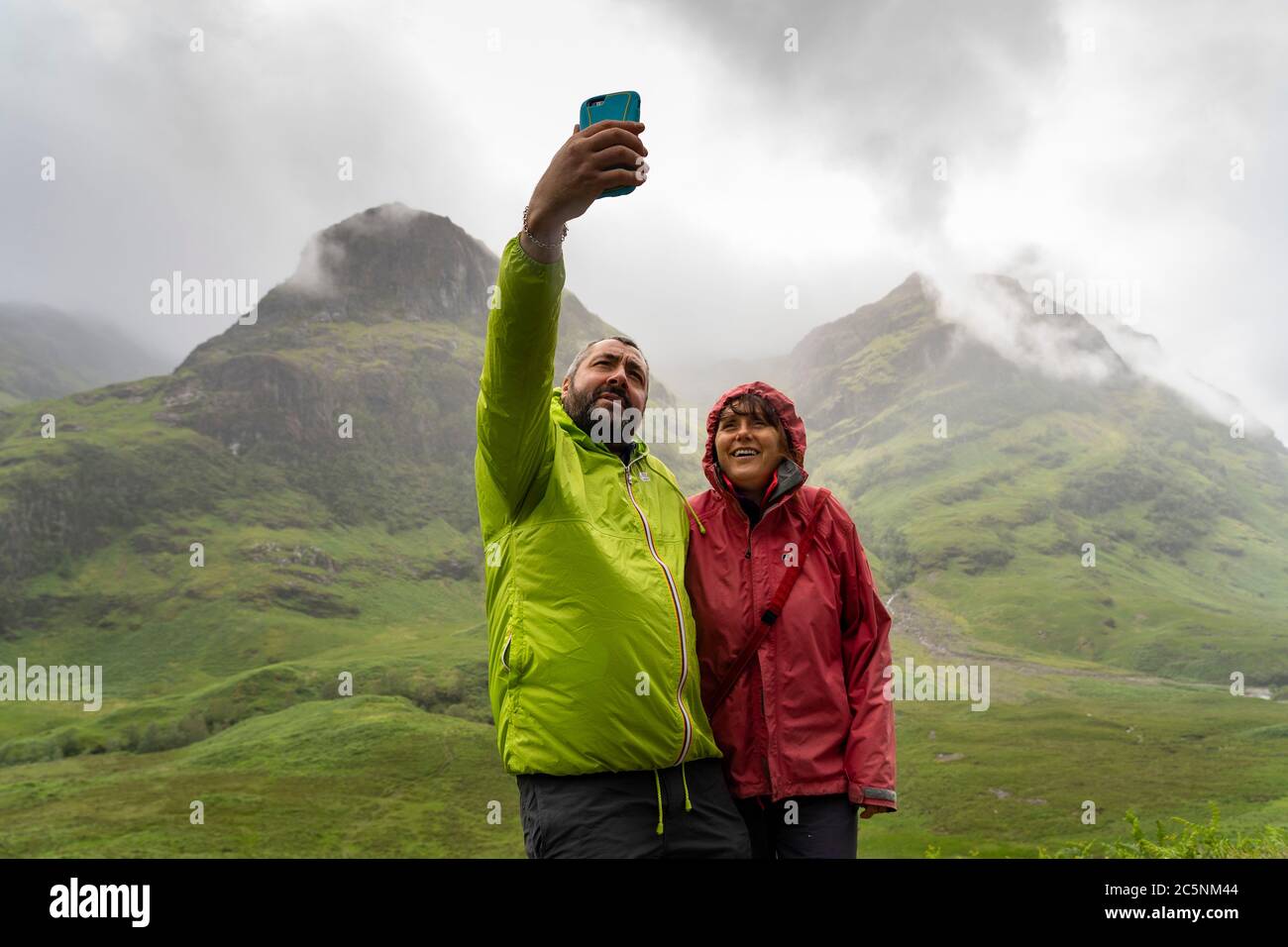 Glen Coe, Scotland, UK. 4 July, 2020. Tourists travel to Glen Coe on first weekend after 5 mile travel restriction was lifted by the Scottish Government. Pictured; couple take selfie photograph with spectacular mountain backdrop in Glen Coe.  Iain Masterton/Alamy Live News Stock Photo