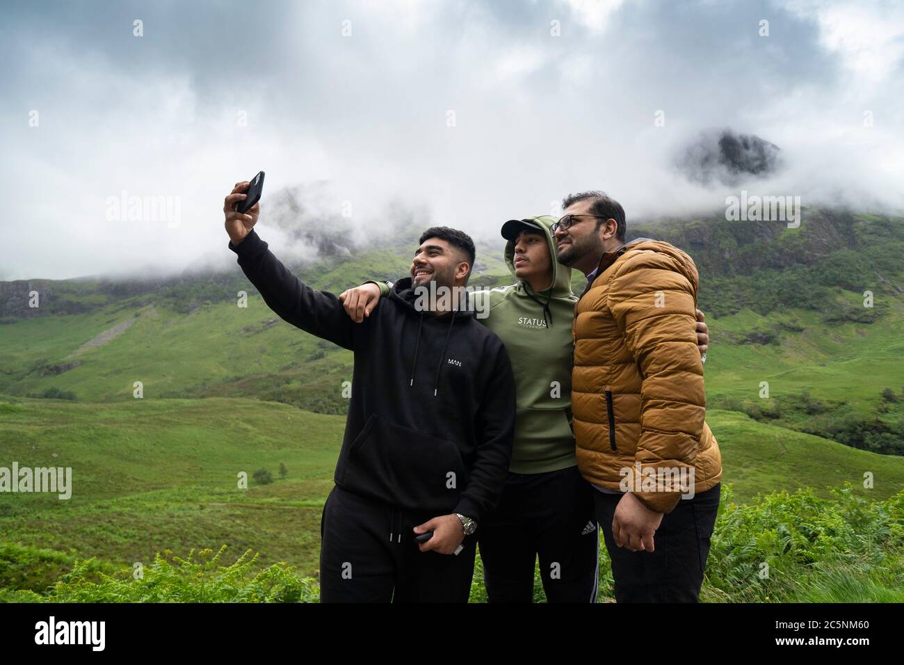 Glen Coe, Scotland, UK. 4 July, 2020. Tourists travel to Glen Coe on first weekend after 5 mile travel restriction was lifted by the Scottish Government. Pictured; Indian day-trippers take selfie photograph with spectacular mountain backdrop in Glen Coe.  Iain Masterton/Alamy Live News Stock Photo