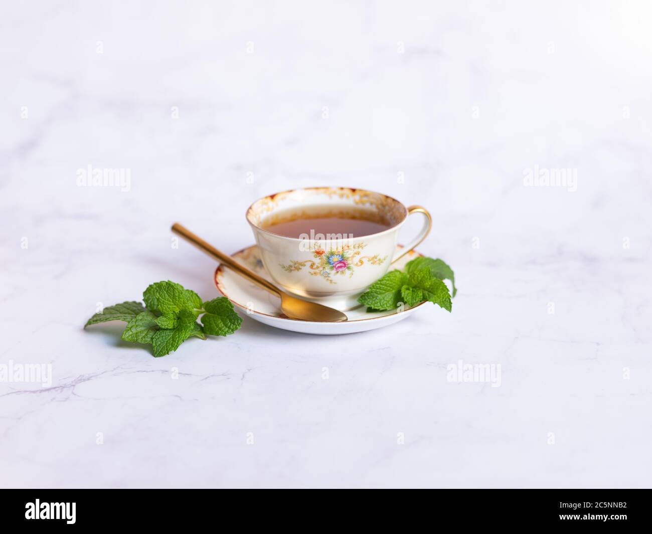 Traditional mint tea cup with spoon and fresh mint on a white marble table Stock Photo