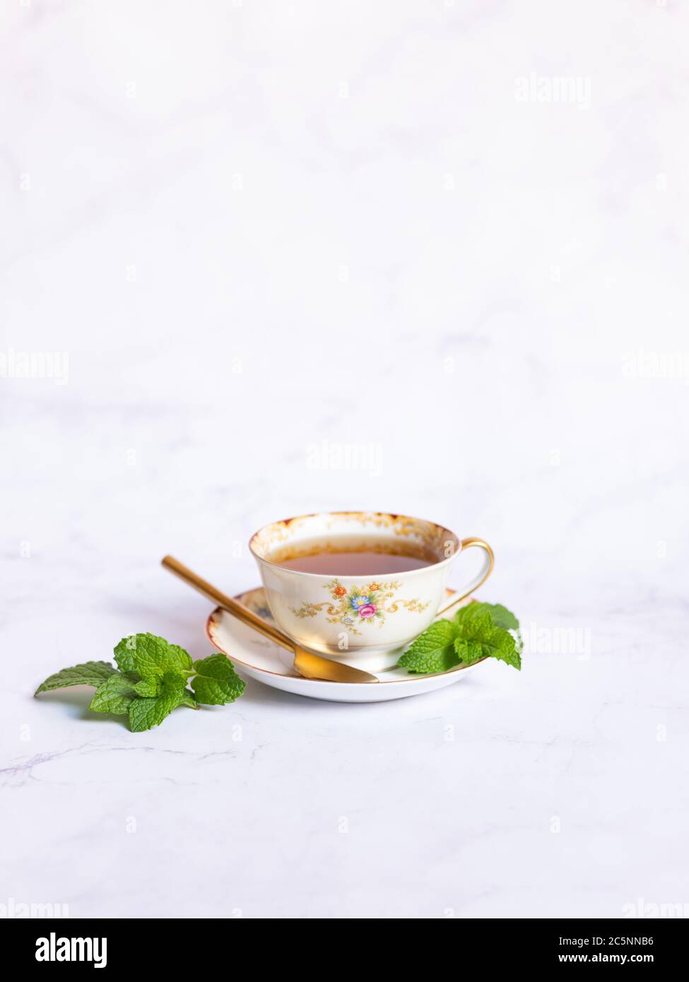 Traditional mint tea cup with spoon and fresh mint on a white marble table Stock Photo