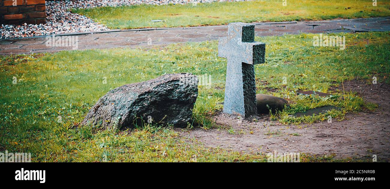 An ancient stone funeral cross and a tombstone on the burial ground near the wall of the old castle. Stock Photo