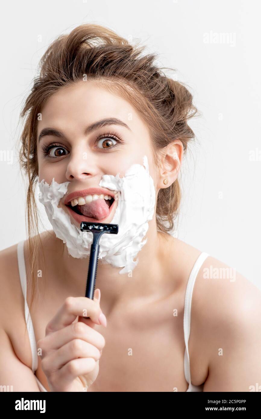 Beautiful young caucasian woman shaving her face by razor on white