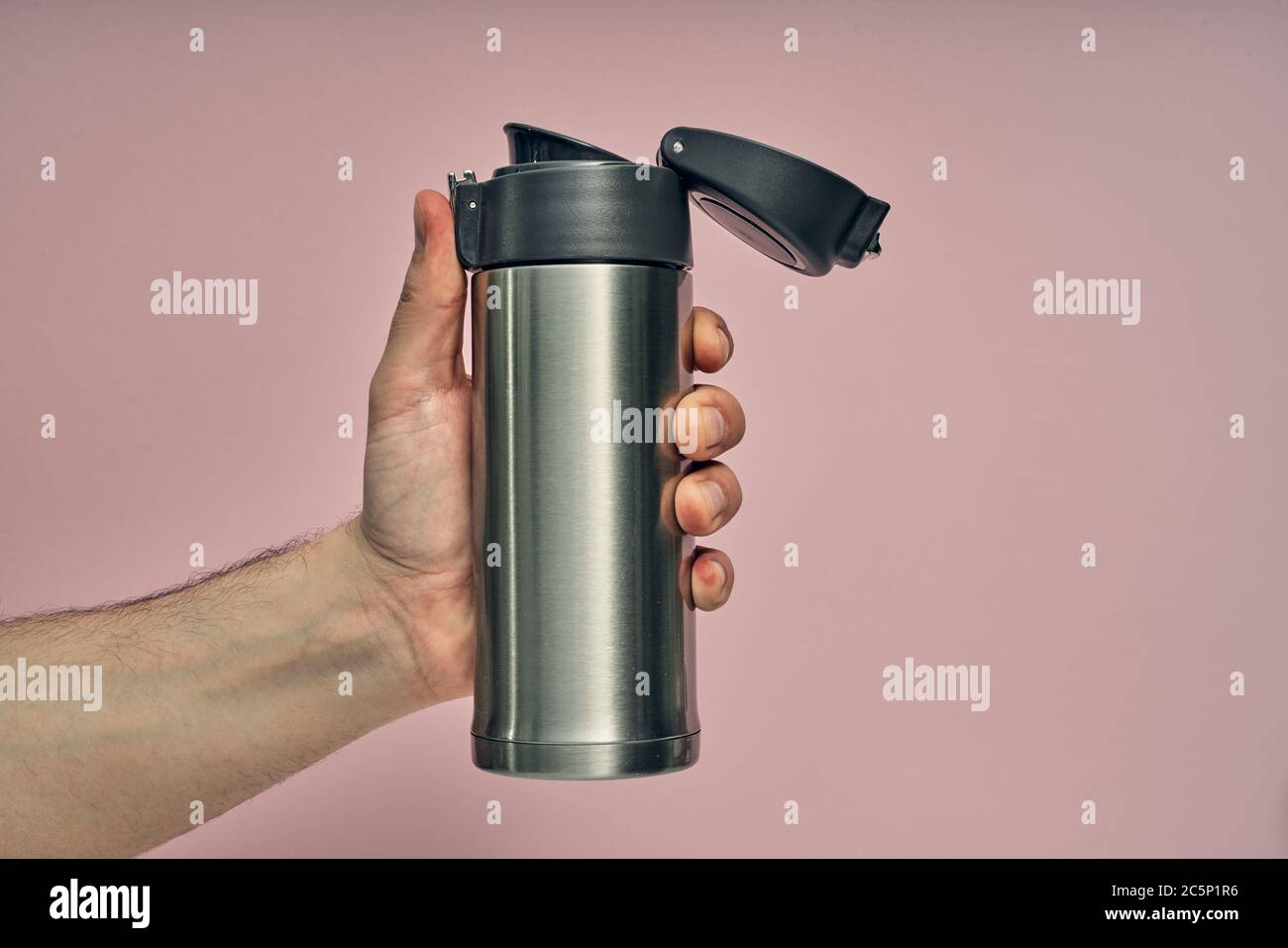 Metal mug thermos in hand on a colored background. Hot drinks on the go. Thermo mug. Stock Photo