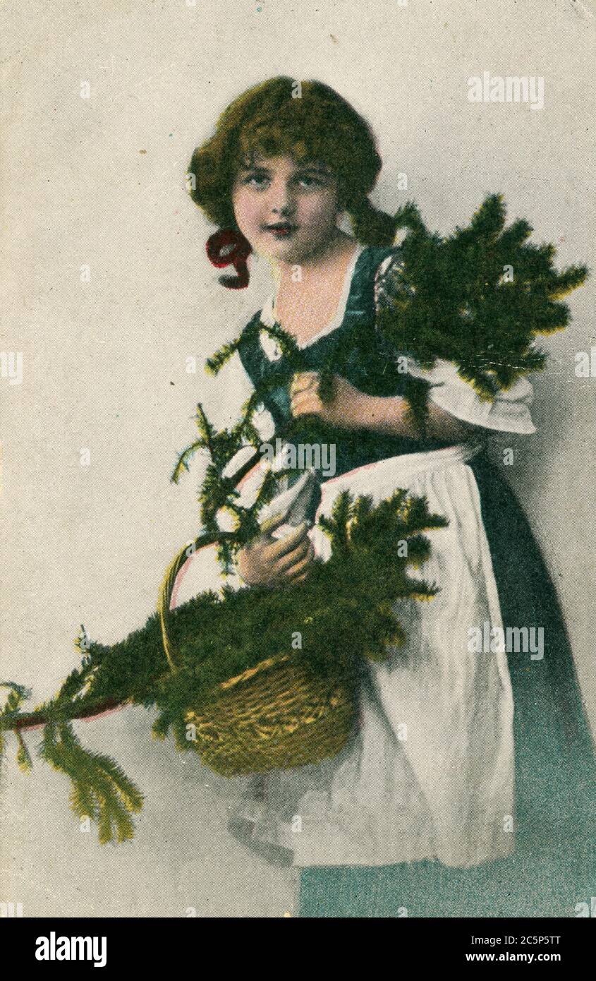 RUSSIA - CIRCA 1910: Retro Christmas postcard depicts a girl with a basket of spruce branches, circa 1910, Russia. Vintage hand-tinted photograph Stock Photo