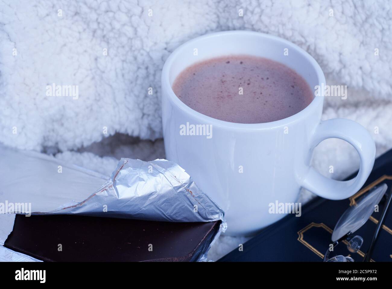 Conceptual image, hot chocolate, dark chocolate with a book and eyeglasses or spectacles on a sheepskin blanket. Stock Photo
