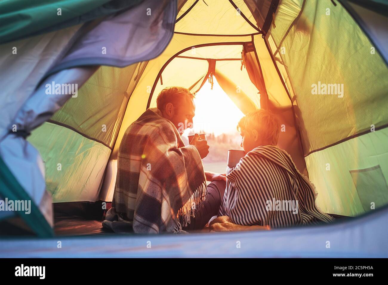 Father and son drink hot tea sitting together in camping tent. Traveling with kids and active people concept image. Stock Photo