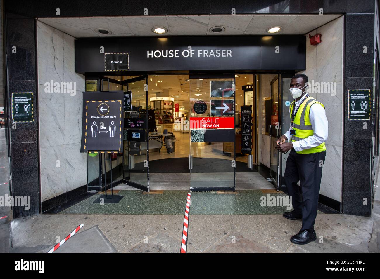 Security wearing a protective face mask directing shoppers into the correct doorway of House of Fraser to maintain social distancing, Kingston, UK Stock Photo