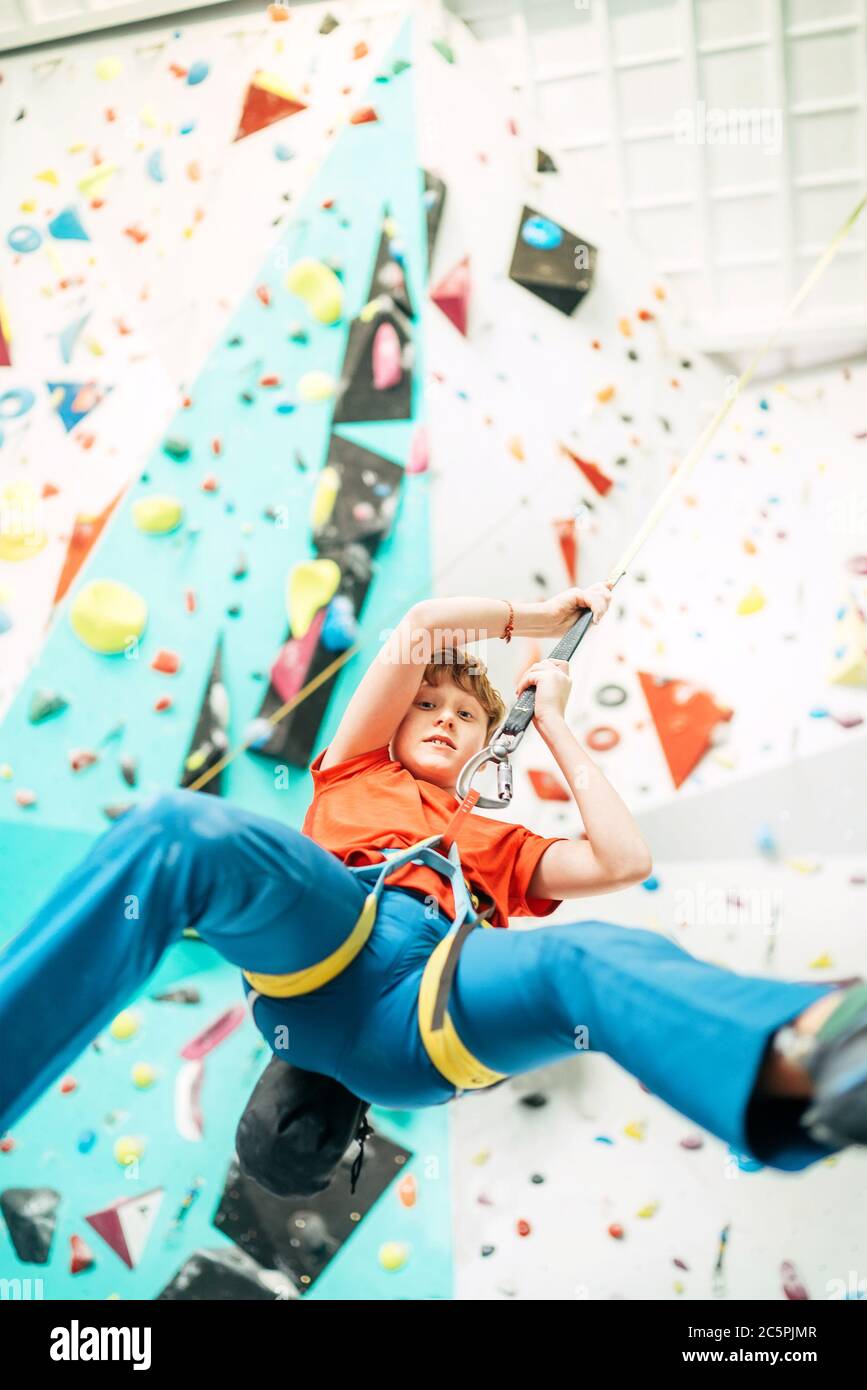 Teenager boy at indoor climbing wall hall. Boy is climbing using an