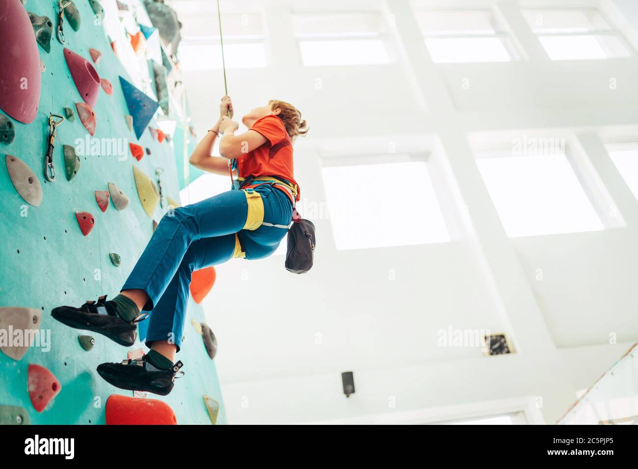 Teenager boy at indoor climbing wall hall. Boy is climbing using a top