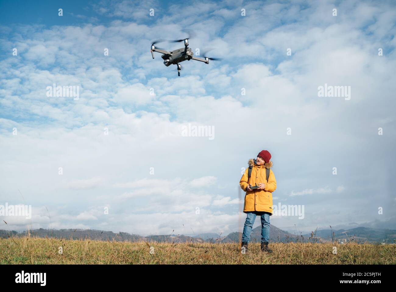 Teenager boy dressed yellow jacket piloting a modern digital drone using remote controller Stock Photo
