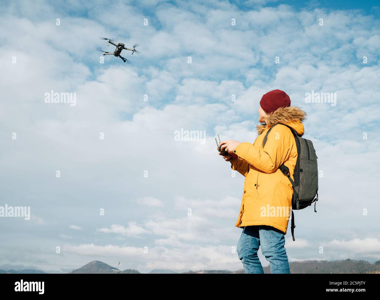 Teenager boy dressed yellow jacket piloting a modern digital drone using remote controller Stock Photo