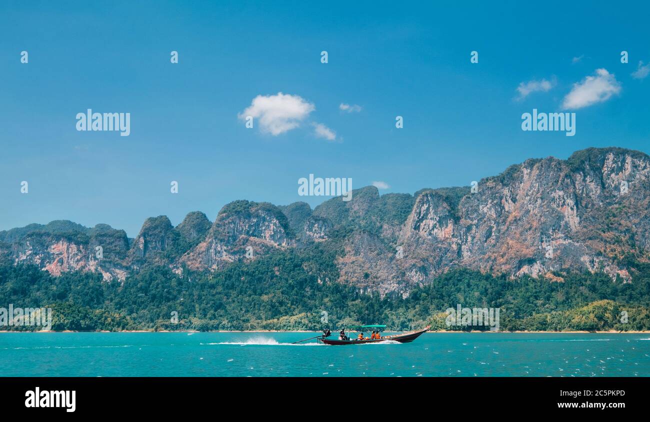 Wooden motorboat vessel using a long propeller shaft sailing with passengers on Thai Khao Sok Lake with foresty mountains around. Exotic countries tra Stock Photo
