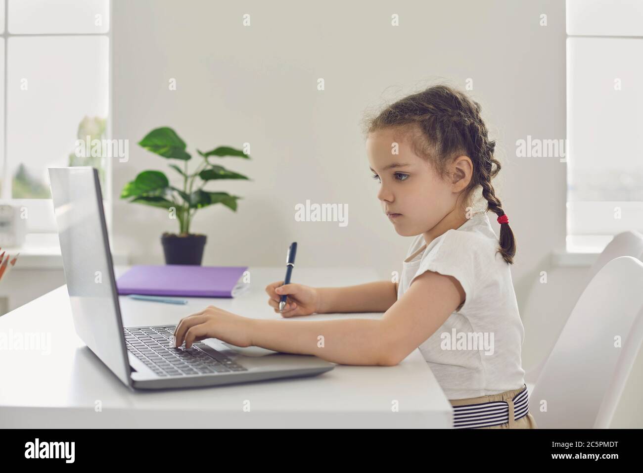 Online learning. Remote school for children. A little girl uses a laptop video lesson while sitting at a table in the room. Stock Photo