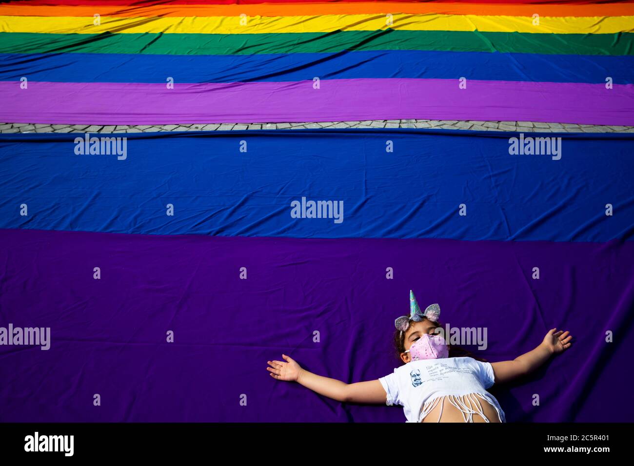 A young girl lies on a huge LGBT flag during the parade day.A group of people marched on the streets of Porto in Portugal to celebrate the 15th Pride Parade. Stock Photo