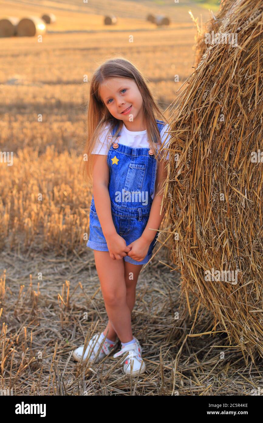 Beautiful little girl stands near a haystack in a summer field Stock ...