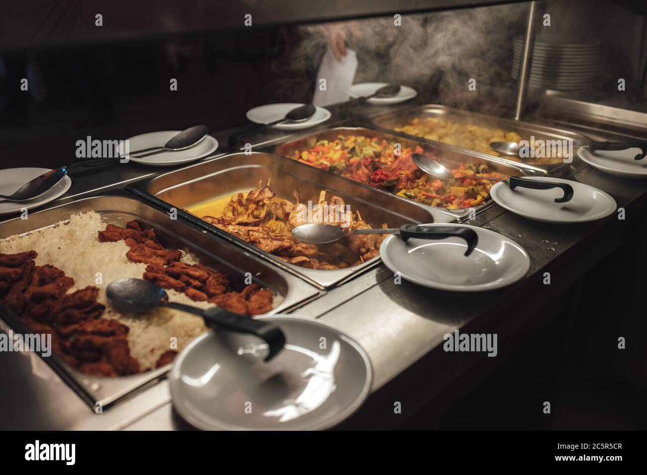 Row of stainless hotel pans on food warmers with various meals. Selfservice buffet table