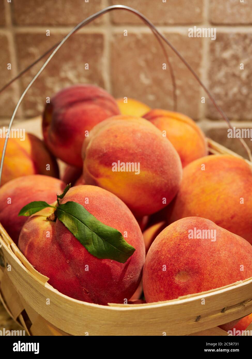 Fresh, ripe cling free peaches a summer fruit in a basket on a kitchen countertop. Stock Photo