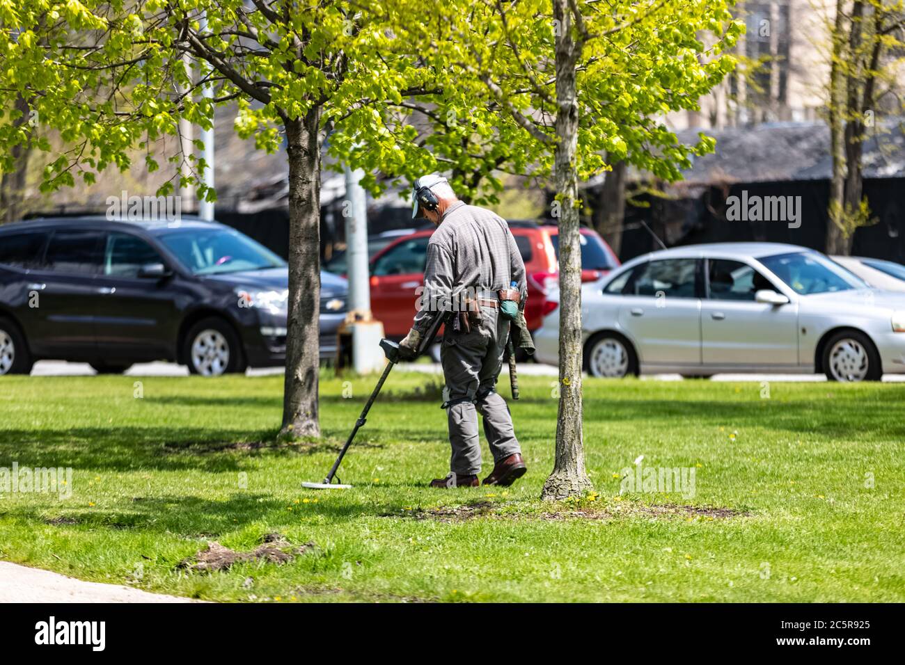 Man using a metal detector  in a park to look for items buried underground. Stock Photo