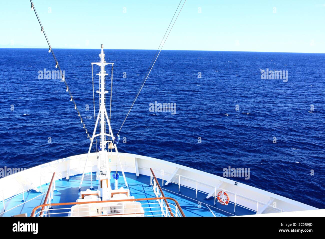 Bow of cruise ship cruising through deep blue ocean with white and blue lower level. Stock Photo