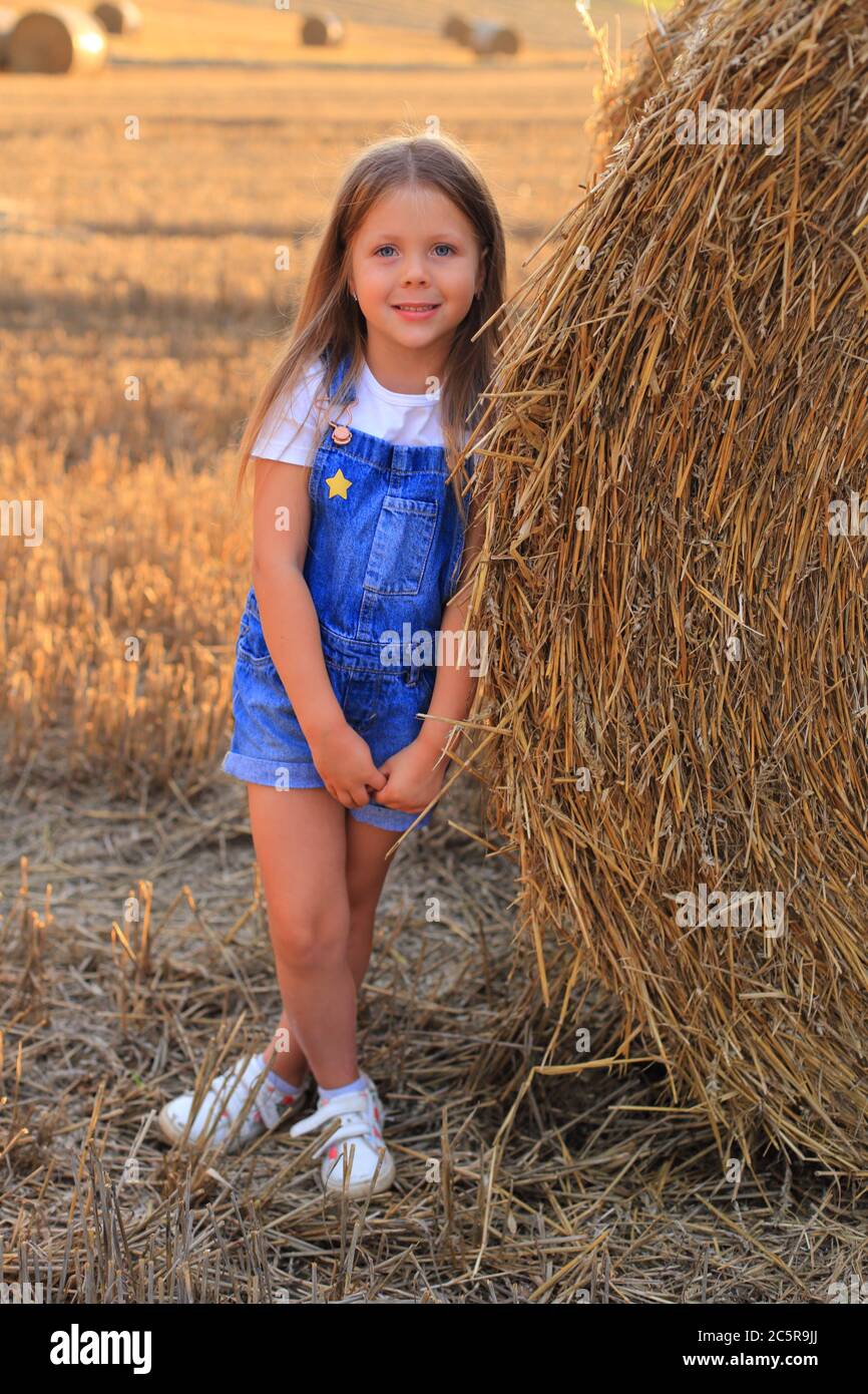 Beautiful little girl stands near a haystack in a summer field Stock ...