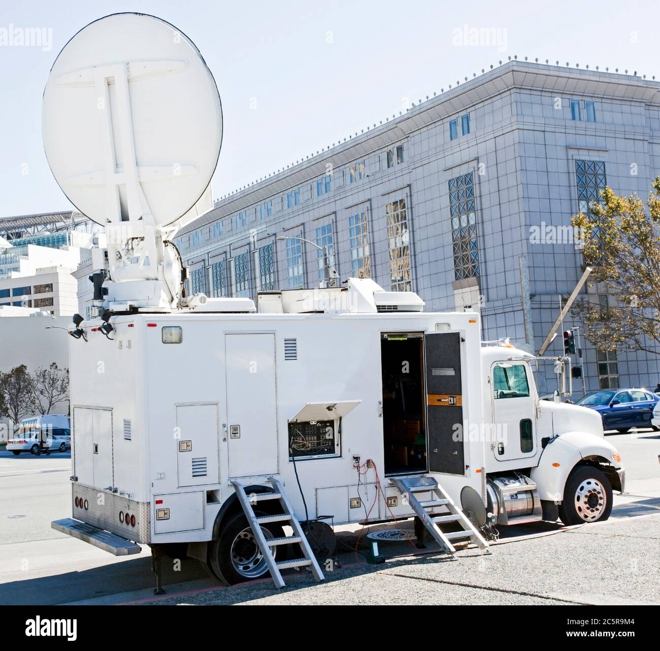 TV production van with satellite dish parked near urban government building. Stock Photo