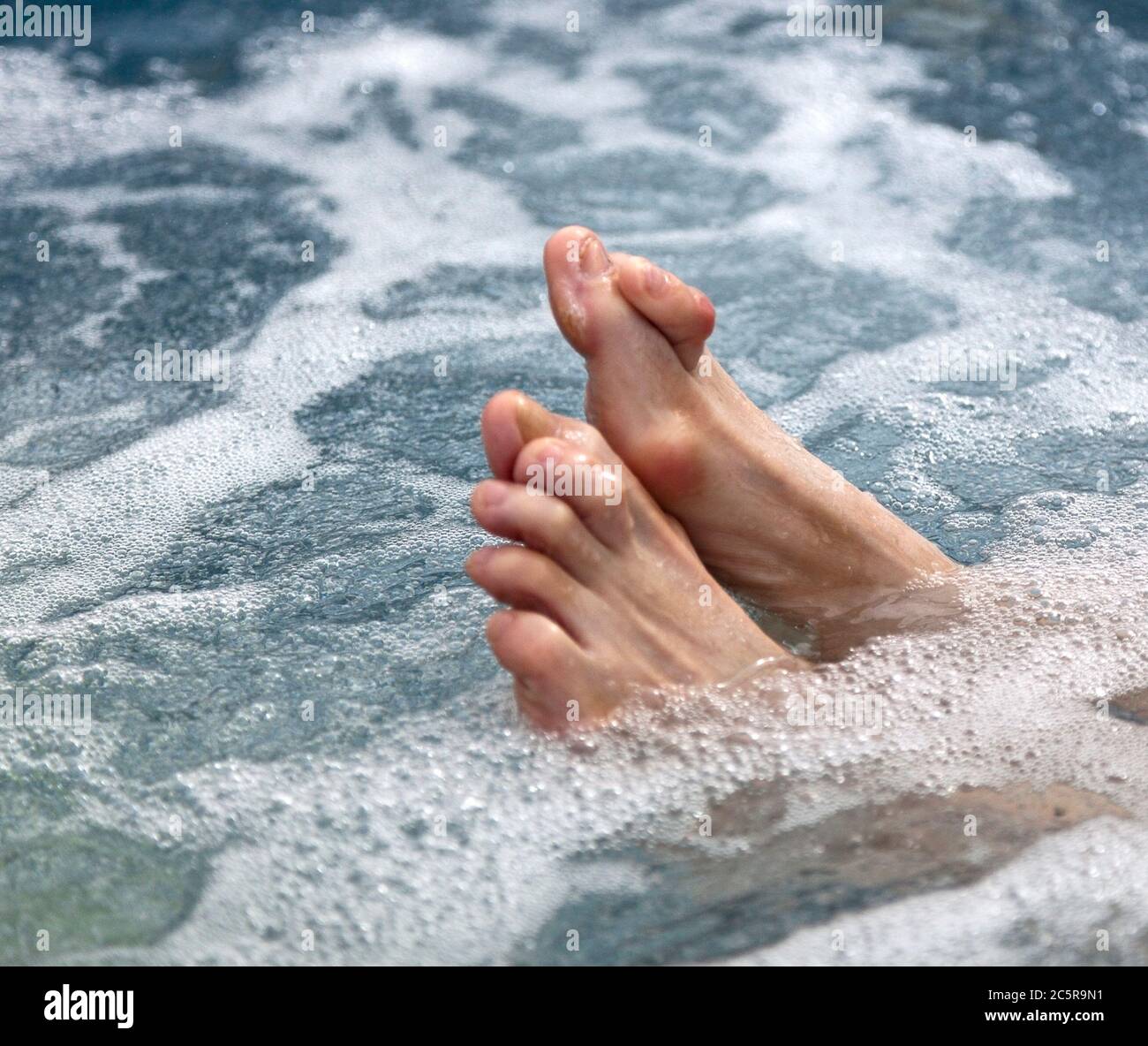 Female feet in hot tub with bone deformities: bunions and hammertoes. Horizontal. Stock Photo