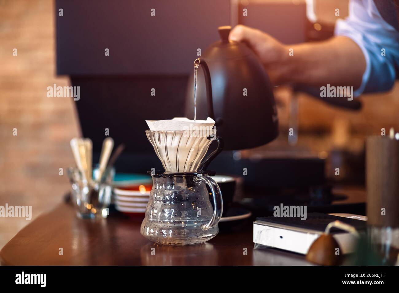 barista pouring boiling water from kettle to drip coffee maker Stock