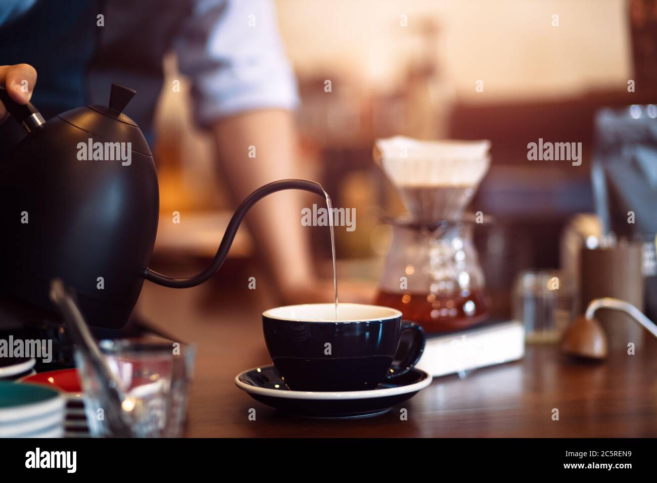 barista pouring boiling water from kettle to drip coffee maker Stock