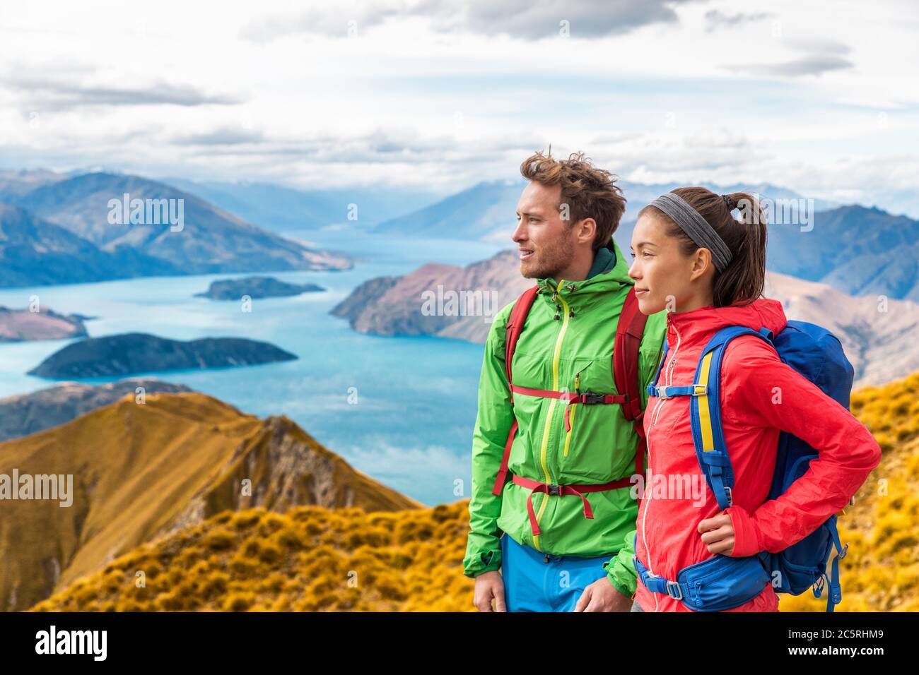 Hiking couple wanderlust adventure and travel concept with hikers relaxing looking at view. Hiking couple tramping up famous hike to Roys Peak on Stock Photo