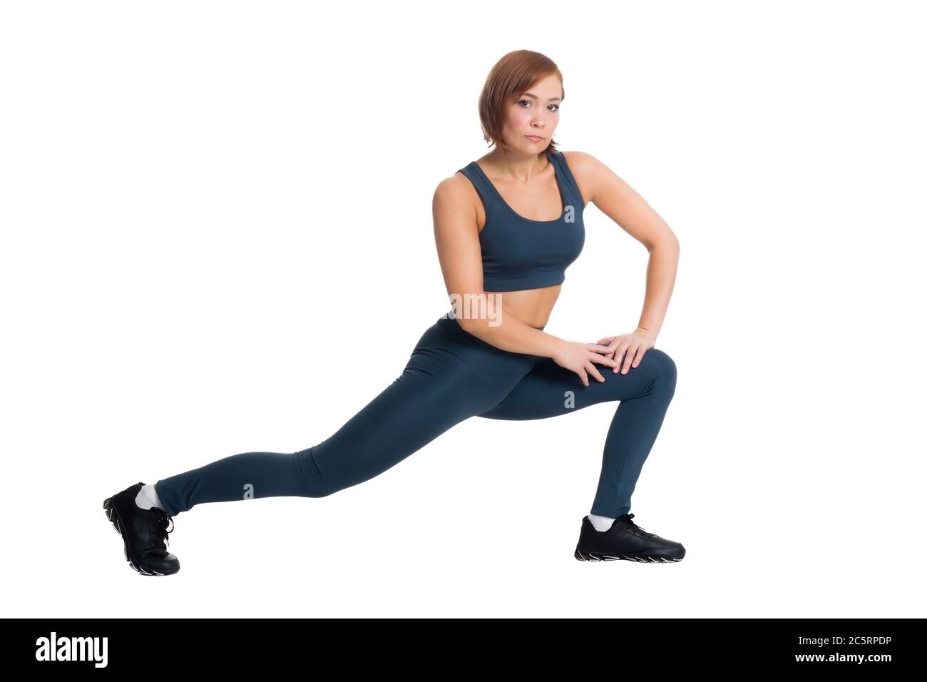 Healthy fitness middle-aged Asian woman in classic blue sportswear, squats on one leg on a white isolate background Stock Photo