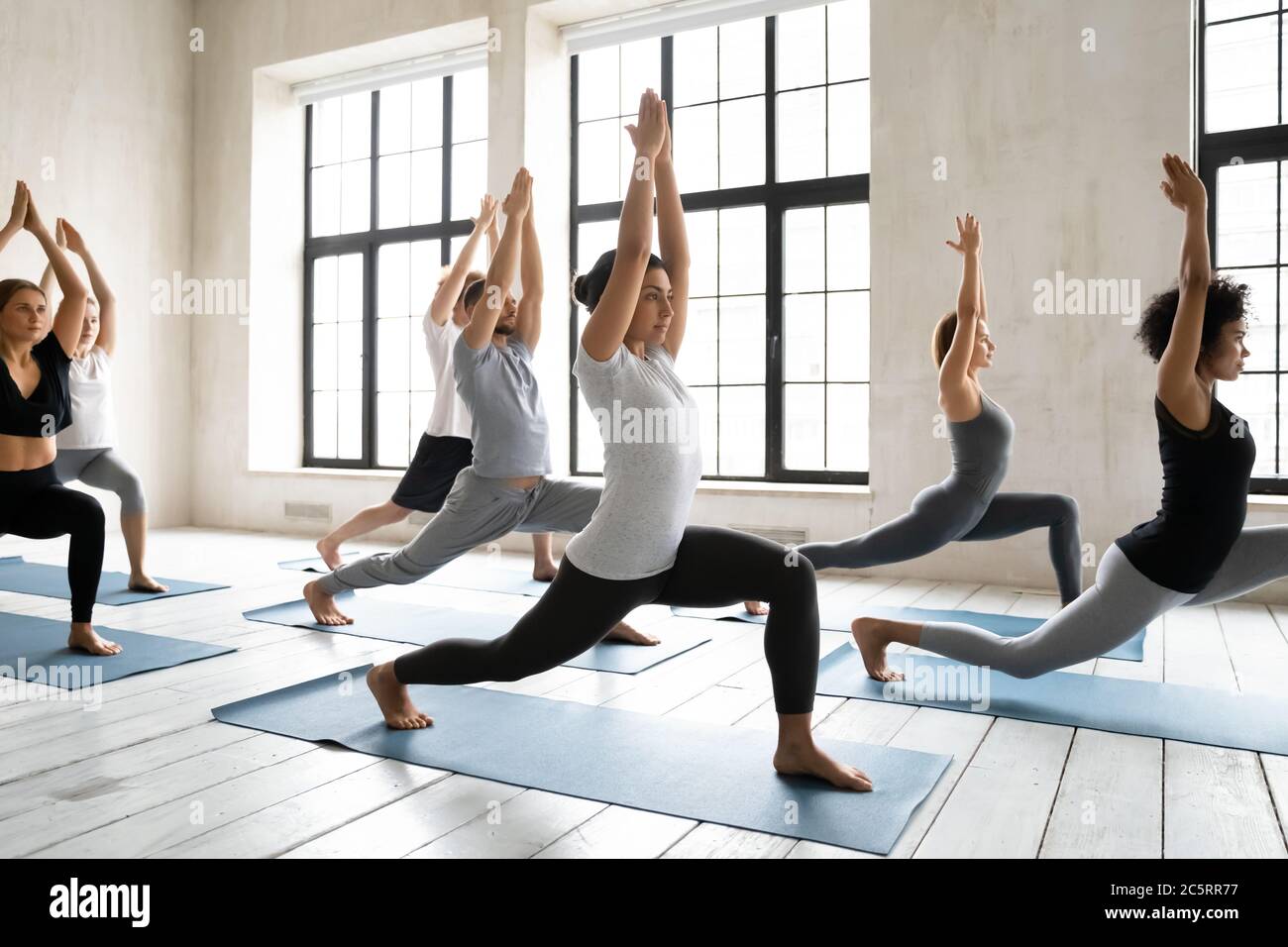 Group of diverse students practicing warrior 1 exercise on yoga class. Stock Photo