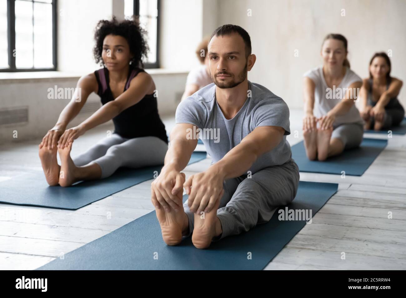 Focused professional male instructor leading yoga class in modern ...