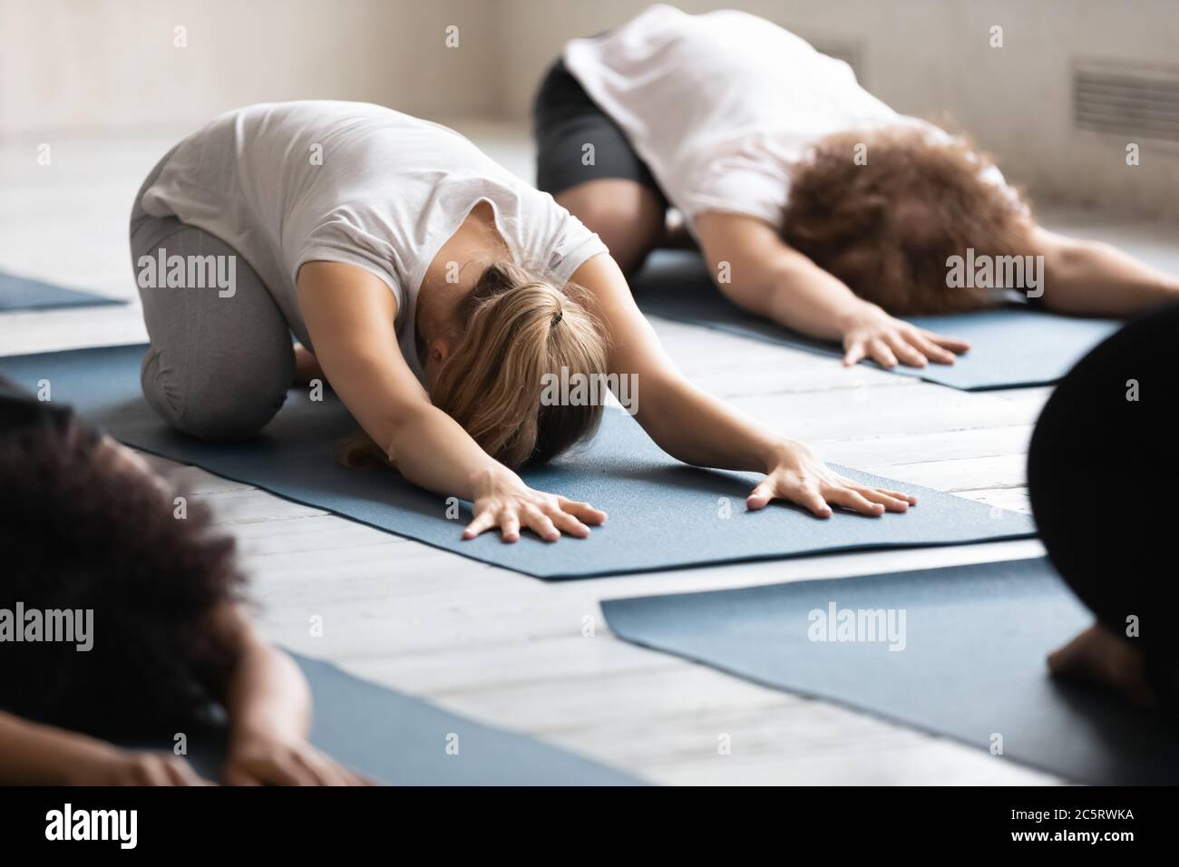 Young female beginner lying on floor mat in balasana pose. Stock Photo