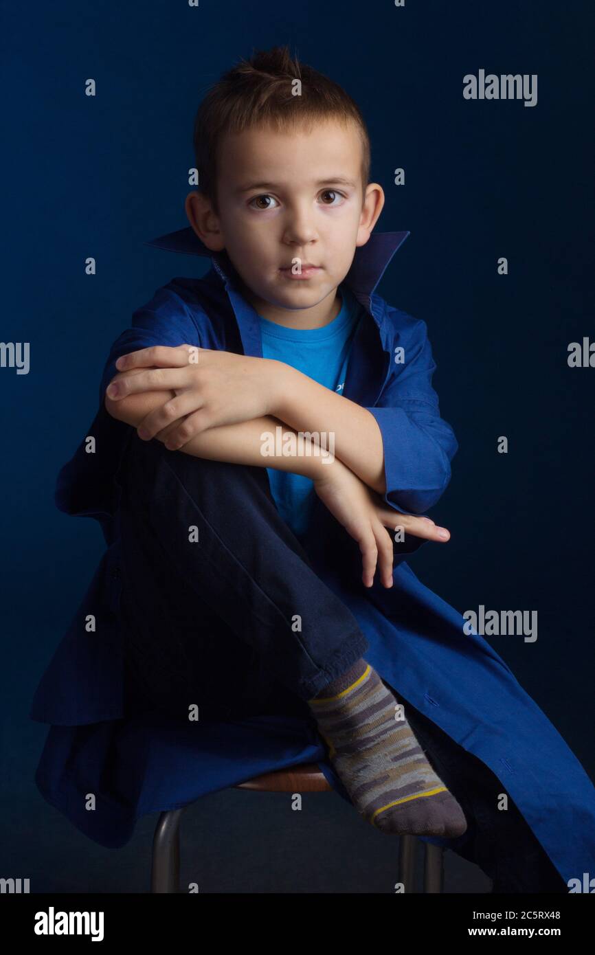 Studio portrait of a boy in a blue classic sweater, sitting on a chair