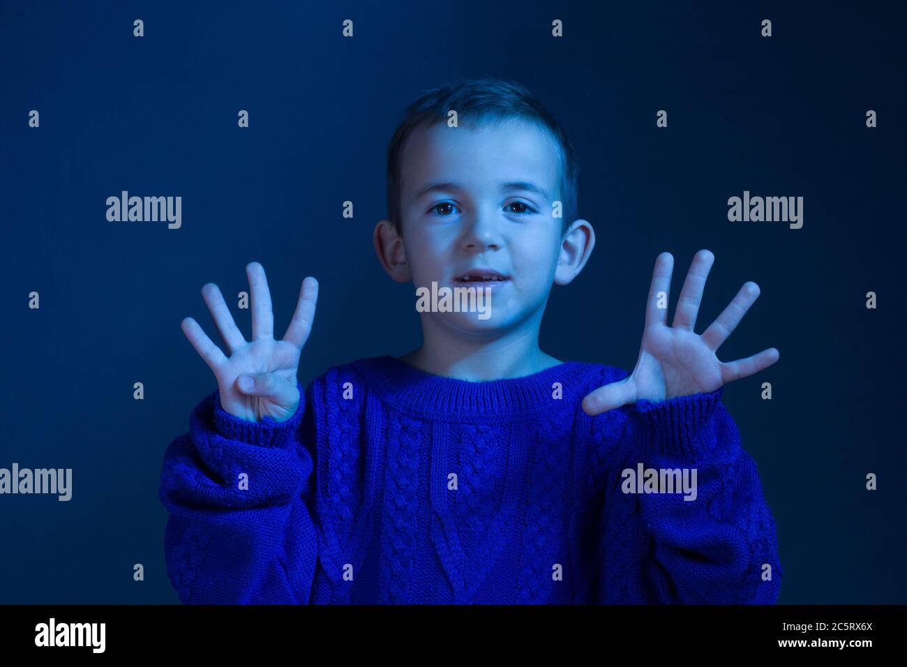 Studio portrait of a brunette Boy who counts on his fingers, shows nine finger, toning in a classic blue color. Stock Photo