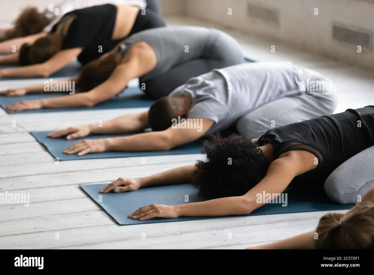 Young diverse people relaxing on floor mat in child pose. Stock Photo