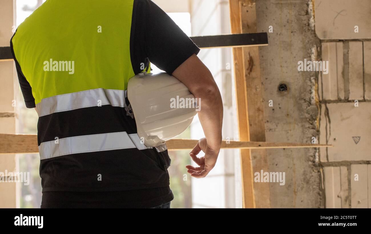 Builder holding helmet on hand, construction site Stock Photo