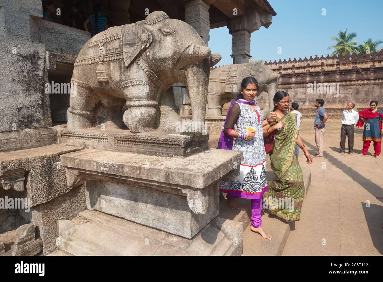 Two women exit the 1000 Pillar (Jain) Temple or Saavira Kambada Basadi in Moodabri (Mudabidri), Karnataka, India, passing two stone elephant statues Stock Photo