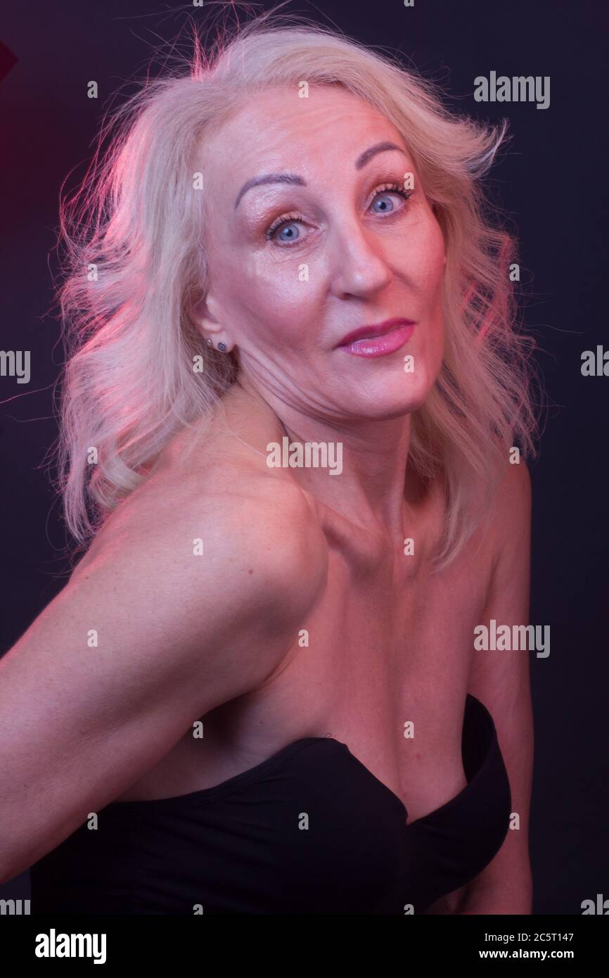 Portrait old woman in a black dress with straps in colorful bright lights.  red and gold color, dark maroon background Stock Photo - Alamy