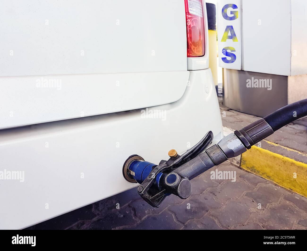 At the gas station, the white car is jammed with liquefied gas, through the pistol of the tanker screwed in behind. Stock Photo