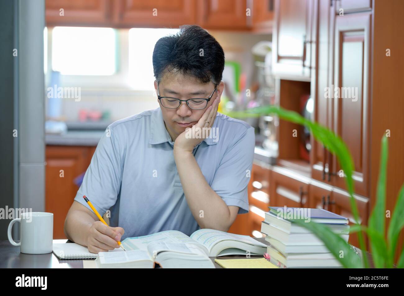 Asian middle-aged man sitting at desk at home, reading a book and studying. Stock Photo