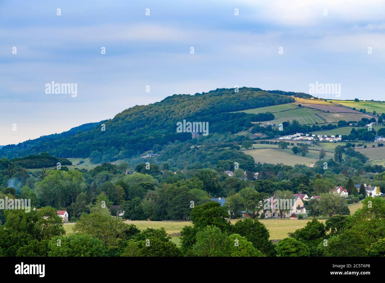 High prominent landmark ridge or escarpment, woodland trees on hillside & houses in scenic valley - view to Chevin Forest Park, Wharfedale, England UK Stock Photo