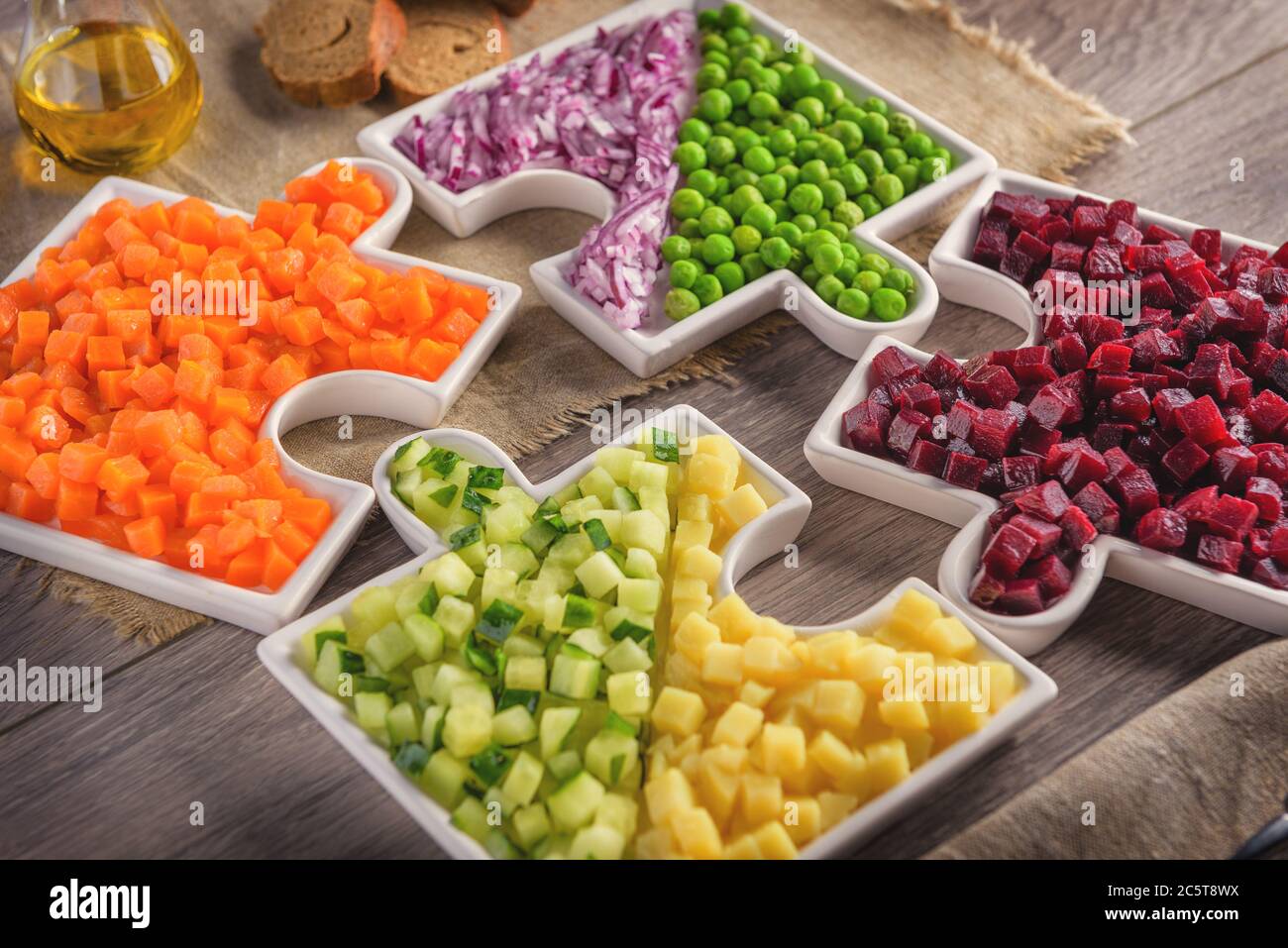 Raw vegetables carrots, peas, onions, cucumber, potatoes, beets cut into cubes lie on plates that are collected in puzzles. Stock Photo