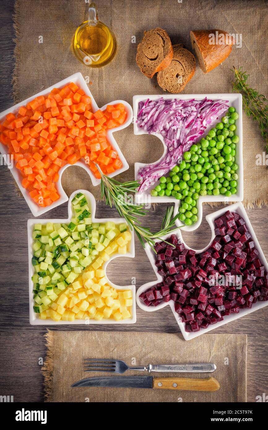 Delicious fresh pieces of vegetables of carrots, cucumber, potatoes, beets and peas close-up with fresh onion and olive oil on a bag cloth on a rustic Stock Photo