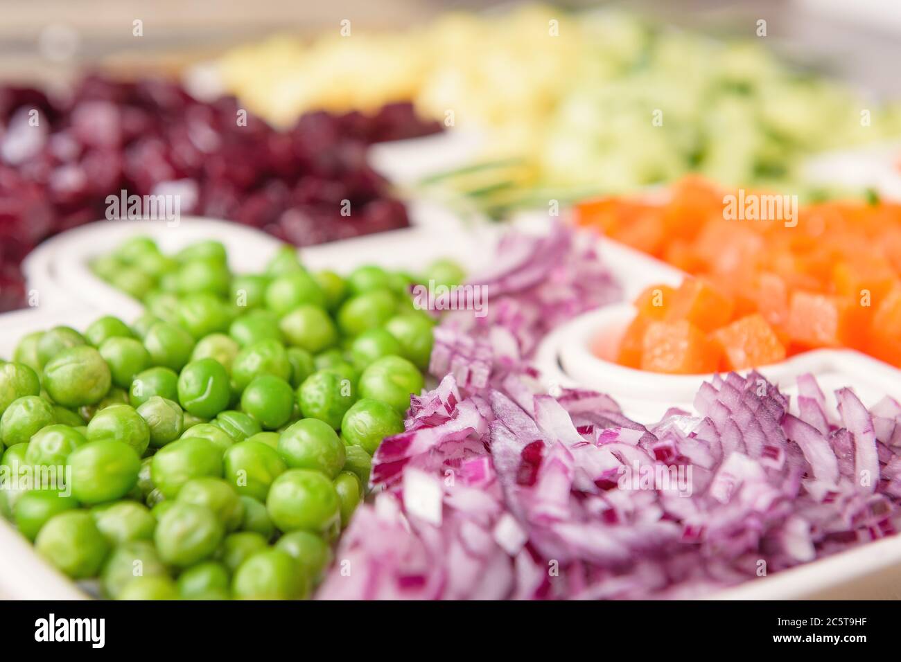 Delicious fresh pieces of vegetables of carrots, cucumber, potatoes, beets and peas close-up with fresh onion and olive oil on a bag cloth on a rustic Stock Photo