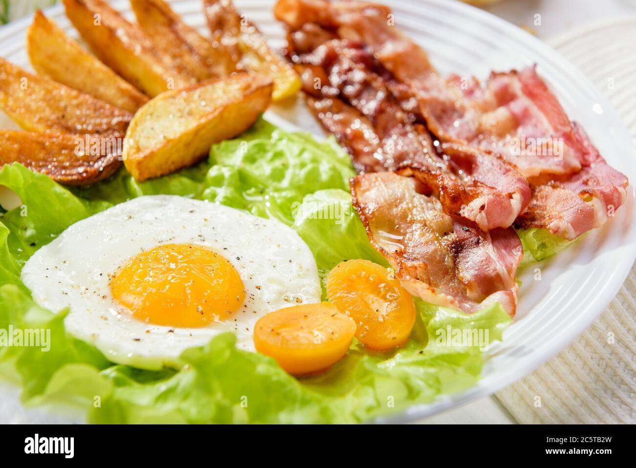 Fried bacon with French fries and a delicate egg, close-up. Stock Photo