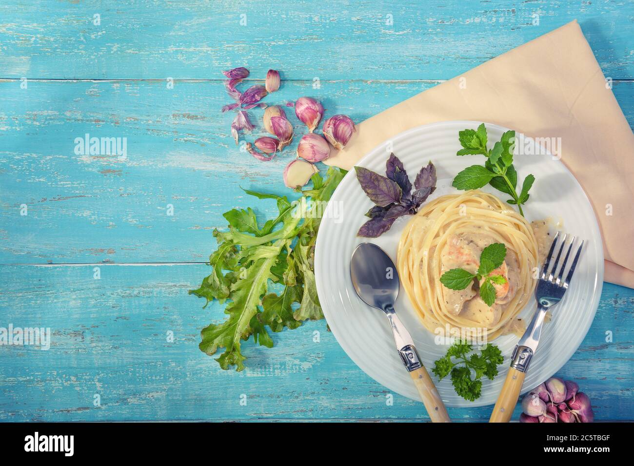 Dish standing on a blue wooden table, a plate with Italian pasta and chicken with a sauce of Provencal herbs, decorated with herbs, salt and garlic. Stock Photo