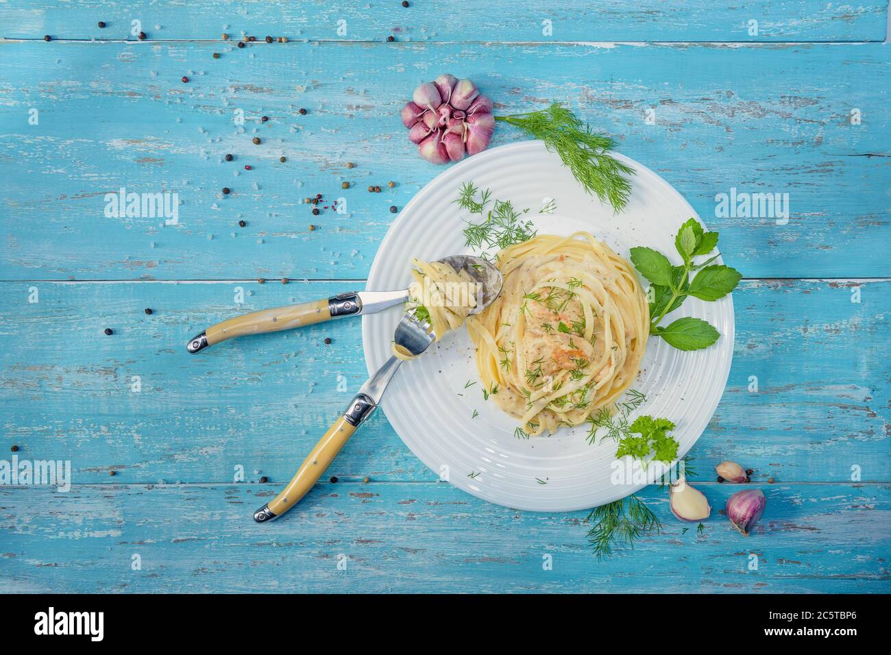 Dish standing on a blue wooden table, a plate with Italian pasta and chicken with a sauce of Provencal herbs, decorated with herbs, salt and garlic. Stock Photo